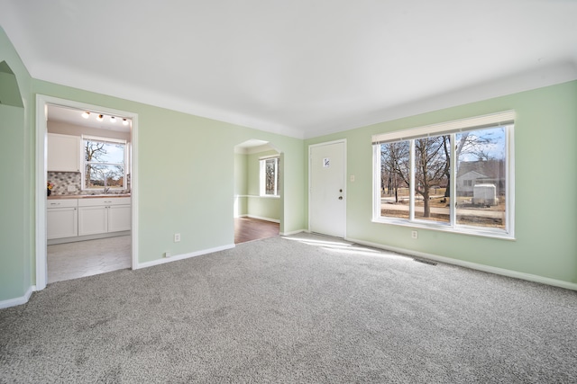 carpeted spare room with arched walkways and baseboards