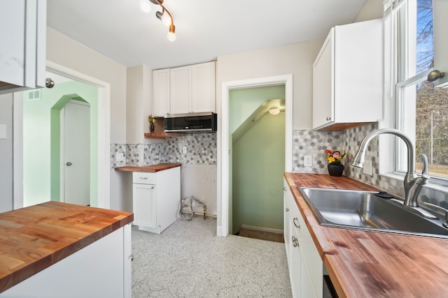 kitchen with butcher block countertops, white cabinetry, stainless steel microwave, and a sink