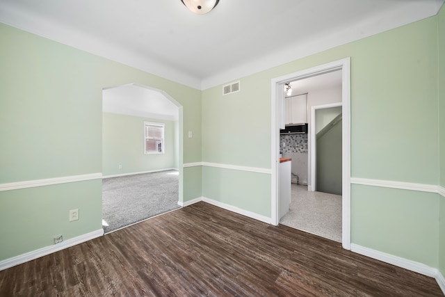 empty room with dark wood finished floors, arched walkways, visible vents, and baseboards