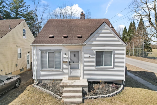 view of front facade with roof with shingles and a chimney