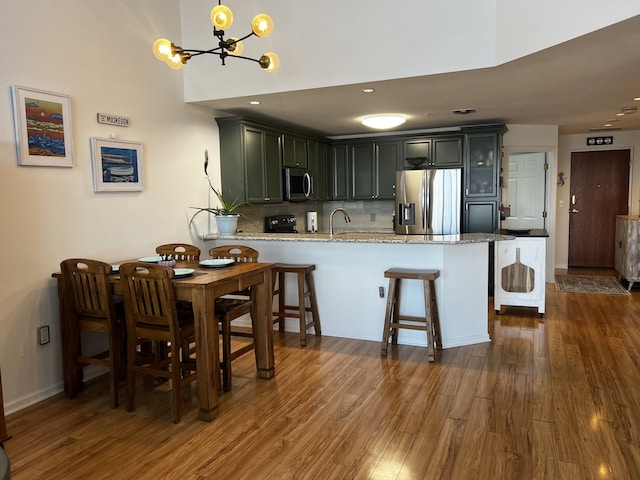 kitchen featuring an inviting chandelier, a peninsula, dark wood-style flooring, a sink, and stainless steel appliances