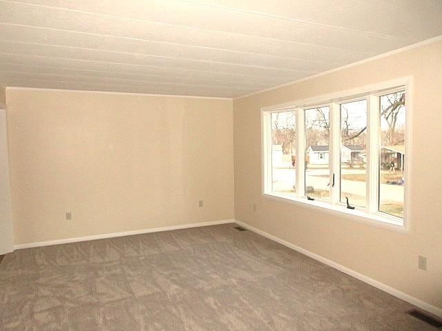 carpeted empty room featuring plenty of natural light, baseboards, and visible vents