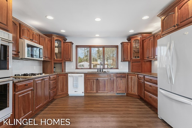 kitchen featuring white appliances, glass insert cabinets, dark wood-style floors, and brown cabinets