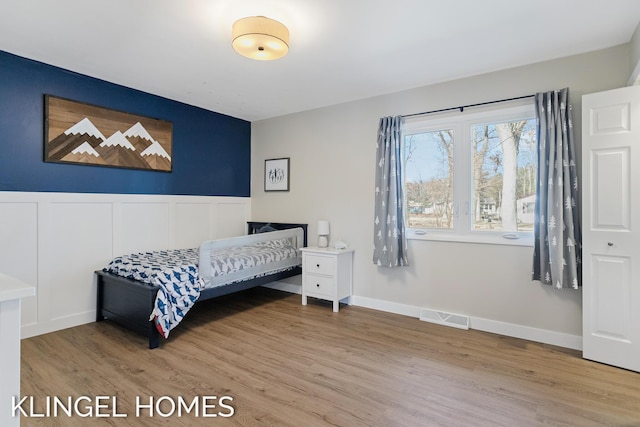 bedroom with visible vents, wood finished floors, and wainscoting