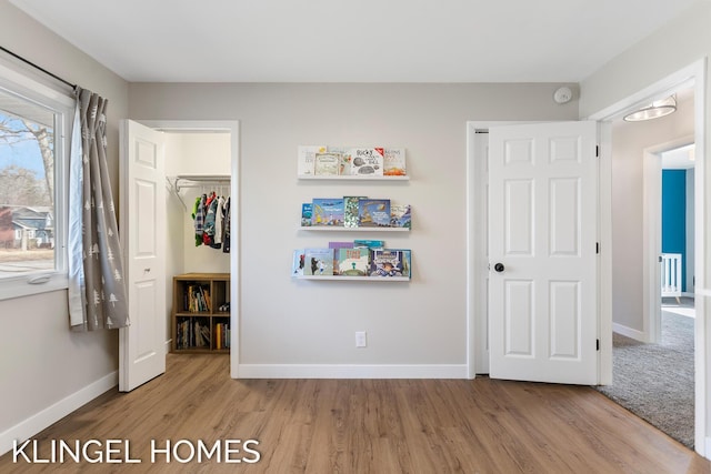 unfurnished bedroom featuring a walk in closet, wood finished floors, a closet, and baseboards