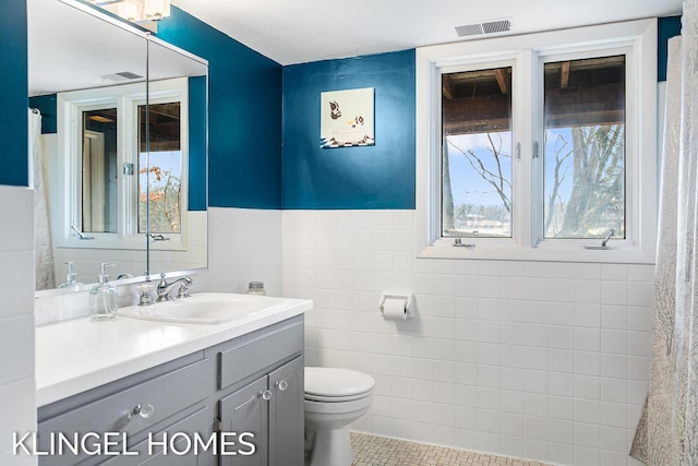 bathroom featuring visible vents, toilet, tile walls, and vanity