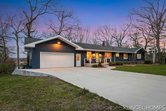 view of front of property featuring a lawn, a chimney, driveway, covered porch, and a garage