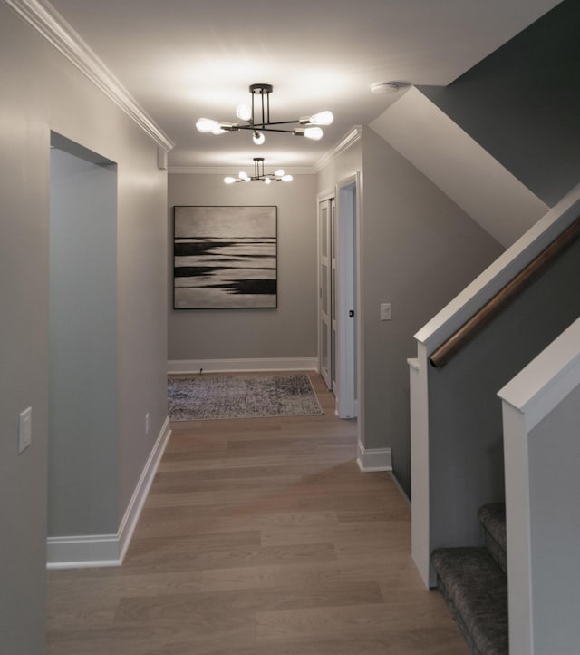 hall featuring light wood-type flooring, an inviting chandelier, ornamental molding, and stairs