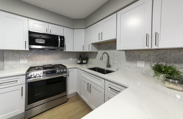 kitchen featuring light wood-style flooring, a sink, appliances with stainless steel finishes, white cabinetry, and tasteful backsplash