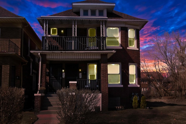 view of front of property featuring a balcony, covered porch, brick siding, and a shingled roof