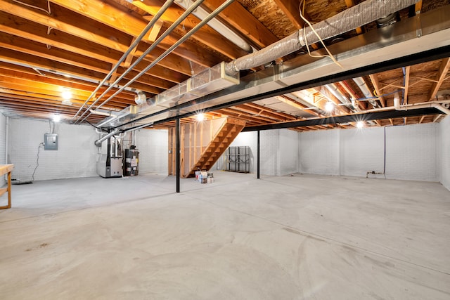 unfinished below grade area featuring brick wall, stairs, water heater, electric panel, and heating unit