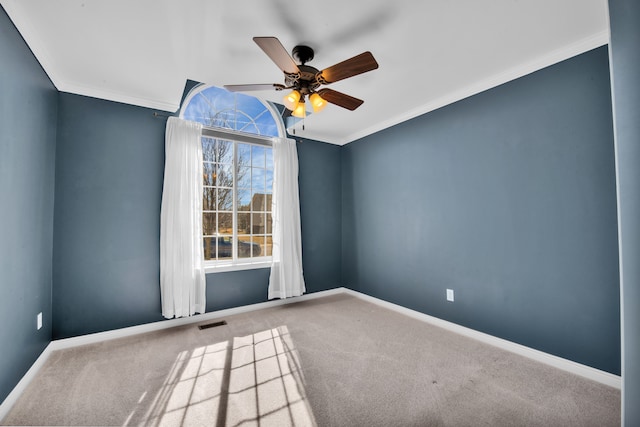 carpeted empty room with visible vents, ceiling fan, crown molding, and baseboards