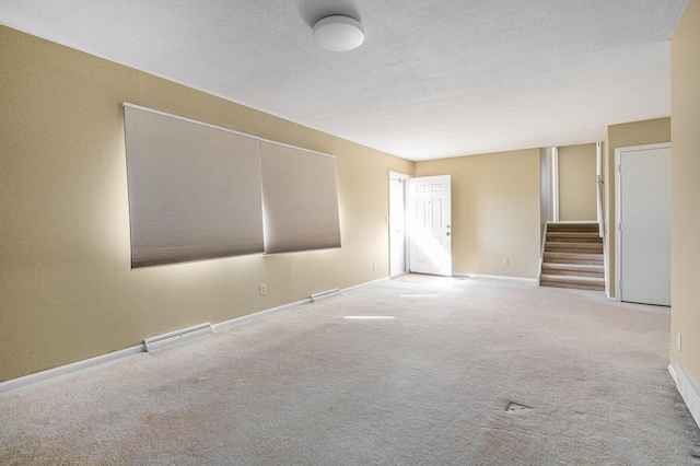 carpeted spare room featuring stairs, baseboards, visible vents, and a textured ceiling