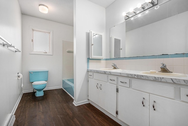 full bath with wood finished floors, double vanity, a sink, toilet, and backsplash