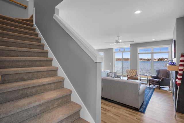 stairway featuring baseboards, a water view, recessed lighting, wood finished floors, and a ceiling fan