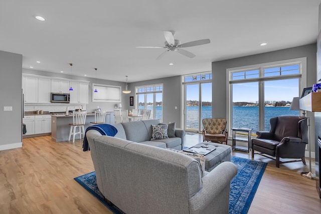 living room featuring baseboards, a water view, recessed lighting, light wood-style flooring, and a ceiling fan