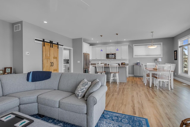 living room with recessed lighting, visible vents, a barn door, and light wood-style floors