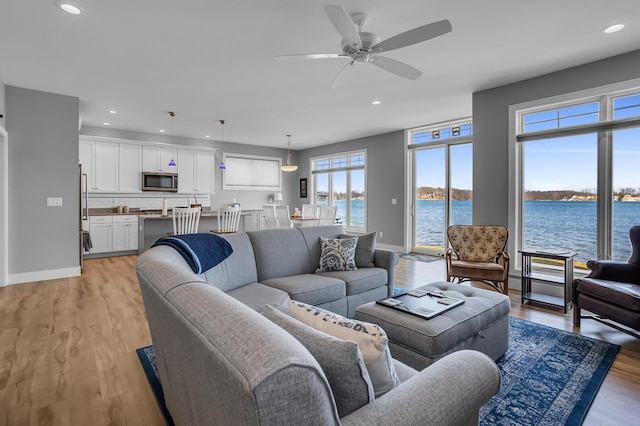 living area with baseboards, light wood-type flooring, a ceiling fan, and a water view