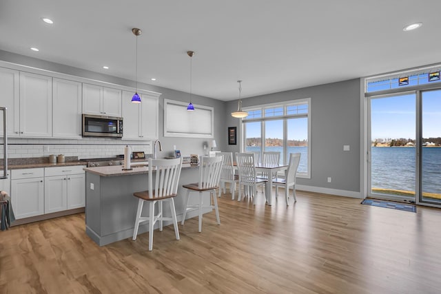 kitchen featuring decorative backsplash, stainless steel microwave, light wood-style flooring, and white cabinets