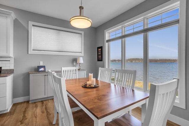 dining space with a wealth of natural light, light wood finished floors, baseboards, and a water view