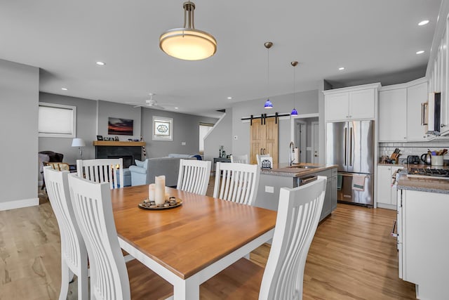 dining space featuring ceiling fan, baseboards, a barn door, recessed lighting, and light wood-style floors