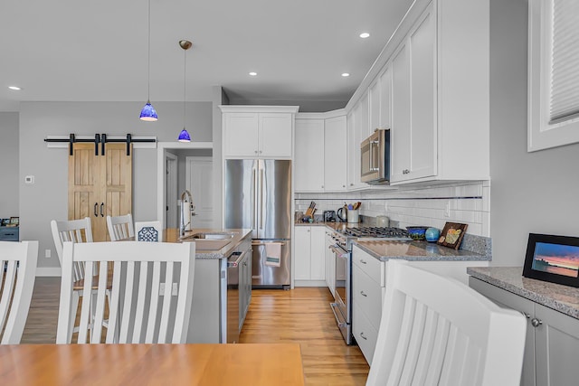 kitchen featuring tasteful backsplash, high quality appliances, light wood-type flooring, an island with sink, and a sink