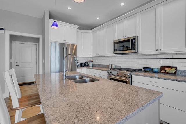 kitchen with light stone counters, a center island with sink, a sink, decorative backsplash, and premium appliances