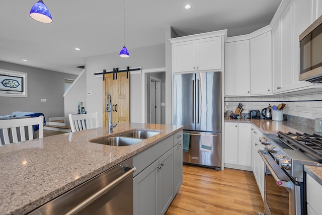 kitchen with light wood finished floors, pendant lighting, a barn door, high end appliances, and a sink