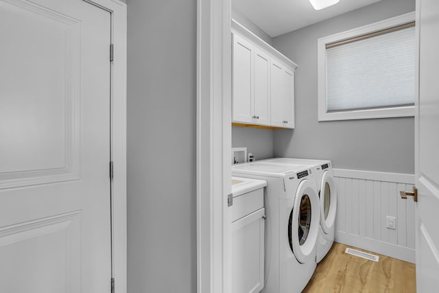 clothes washing area with a wainscoted wall, visible vents, light wood-style flooring, cabinet space, and washing machine and clothes dryer