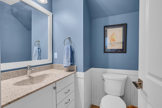 half bathroom featuring a wainscoted wall, toilet, and vanity