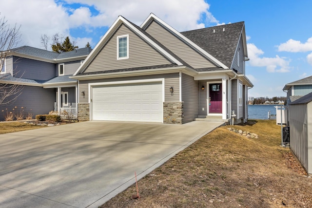 craftsman-style house featuring a water view, stone siding, driveway, and a shingled roof