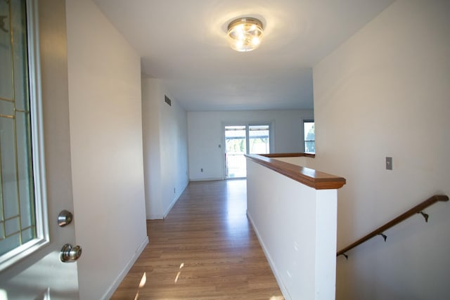 hallway featuring light wood-style flooring, an upstairs landing, visible vents, and baseboards