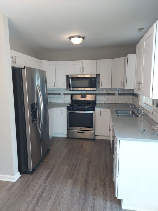 kitchen with dark wood-style flooring, backsplash, stainless steel appliances, and a sink