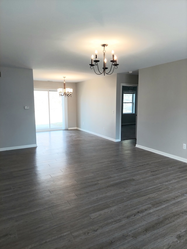 spare room with baseboards, a notable chandelier, a healthy amount of sunlight, and dark wood finished floors