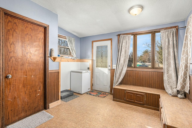 laundry room featuring a wainscoted wall, wood walls, light floors, laundry area, and a textured ceiling