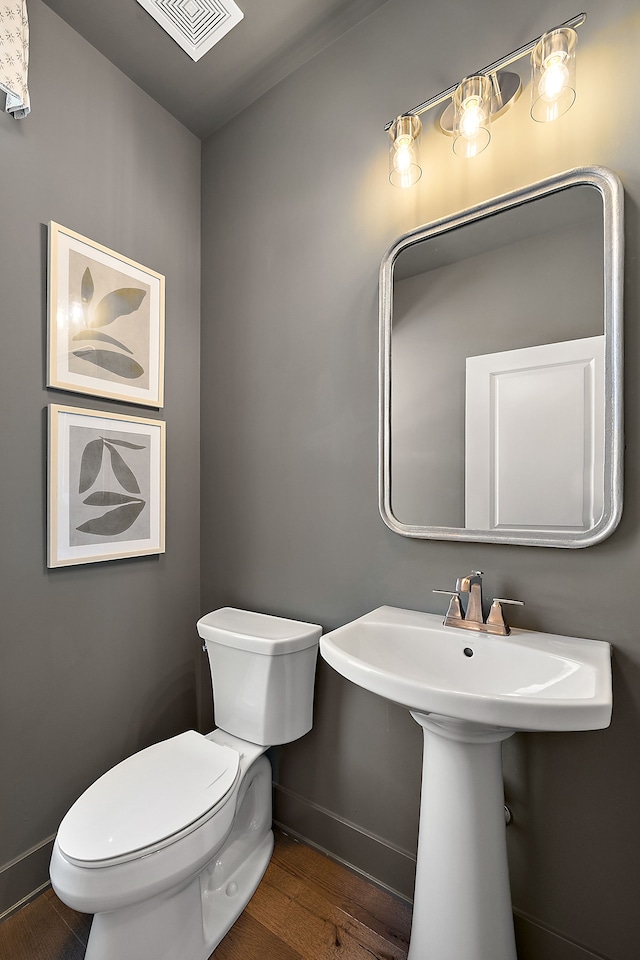 half bath with visible vents, baseboards, toilet, and wood finished floors