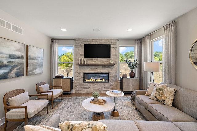 living room with a stone fireplace, wood finished floors, visible vents, and a healthy amount of sunlight