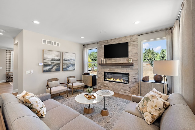 living area featuring a stone fireplace, recessed lighting, wood finished floors, and visible vents