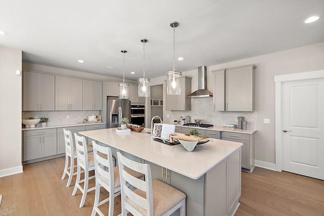 kitchen with light wood-style flooring, wall chimney exhaust hood, stainless steel appliances, and gray cabinetry