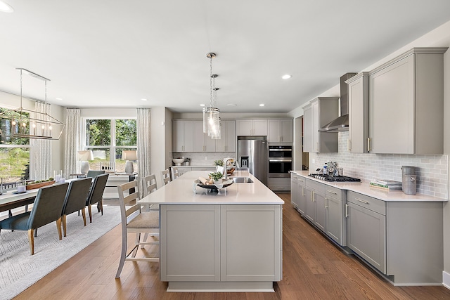 kitchen featuring gray cabinetry, stainless steel appliances, light countertops, and wall chimney range hood