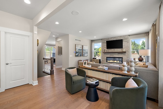 living room with plenty of natural light, light wood-style floors, and a stone fireplace