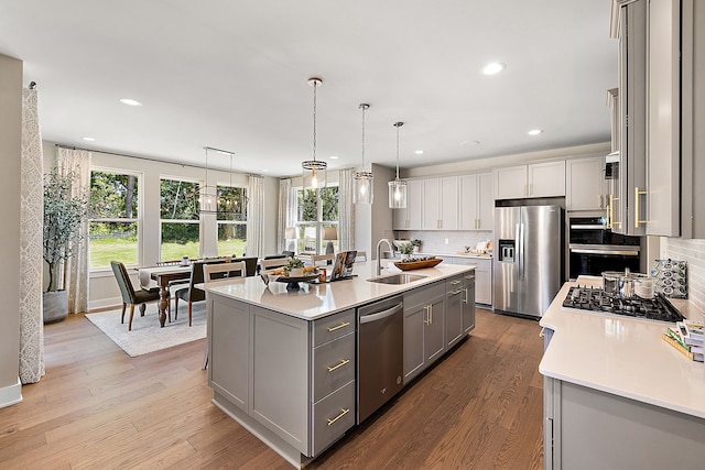 kitchen with light countertops, gray cabinets, appliances with stainless steel finishes, wood finished floors, and a sink