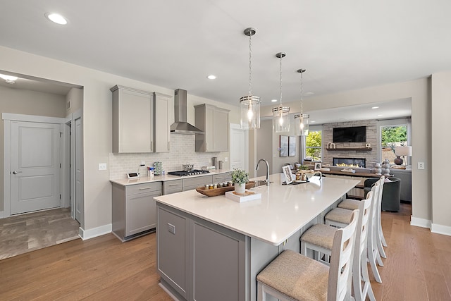 kitchen featuring tasteful backsplash, gray cabinetry, wall chimney range hood, a breakfast bar area, and light countertops