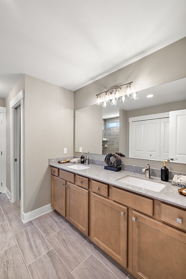 bathroom with double vanity, tiled shower, baseboards, and a sink