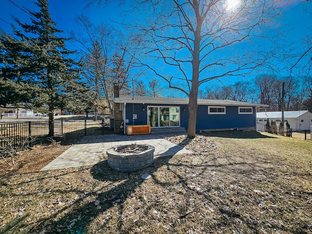 rear view of property featuring a fire pit, fence, a lawn, a chimney, and a patio