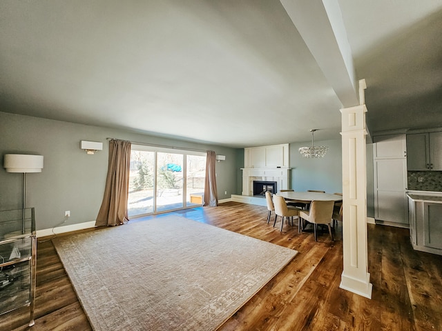 living room with dark wood finished floors, a fireplace with raised hearth, baseboards, and ornate columns