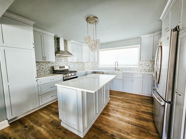 kitchen featuring dark wood-type flooring, wall chimney range hood, light countertops, decorative backsplash, and appliances with stainless steel finishes