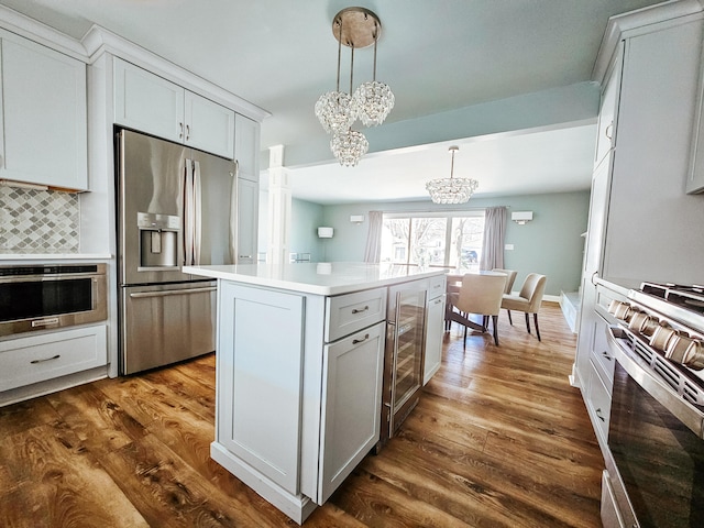 kitchen featuring a notable chandelier, tasteful backsplash, a kitchen island, stainless steel appliances, and dark wood-style flooring