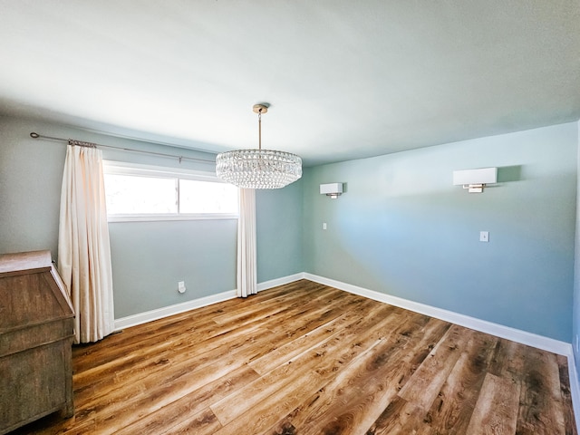 unfurnished dining area with a wall mounted air conditioner, baseboards, wood finished floors, and a chandelier