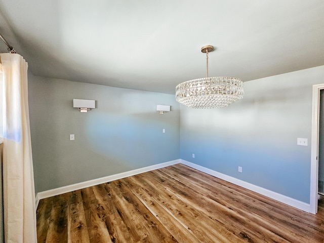 unfurnished room with baseboards, a notable chandelier, and dark wood-style floors